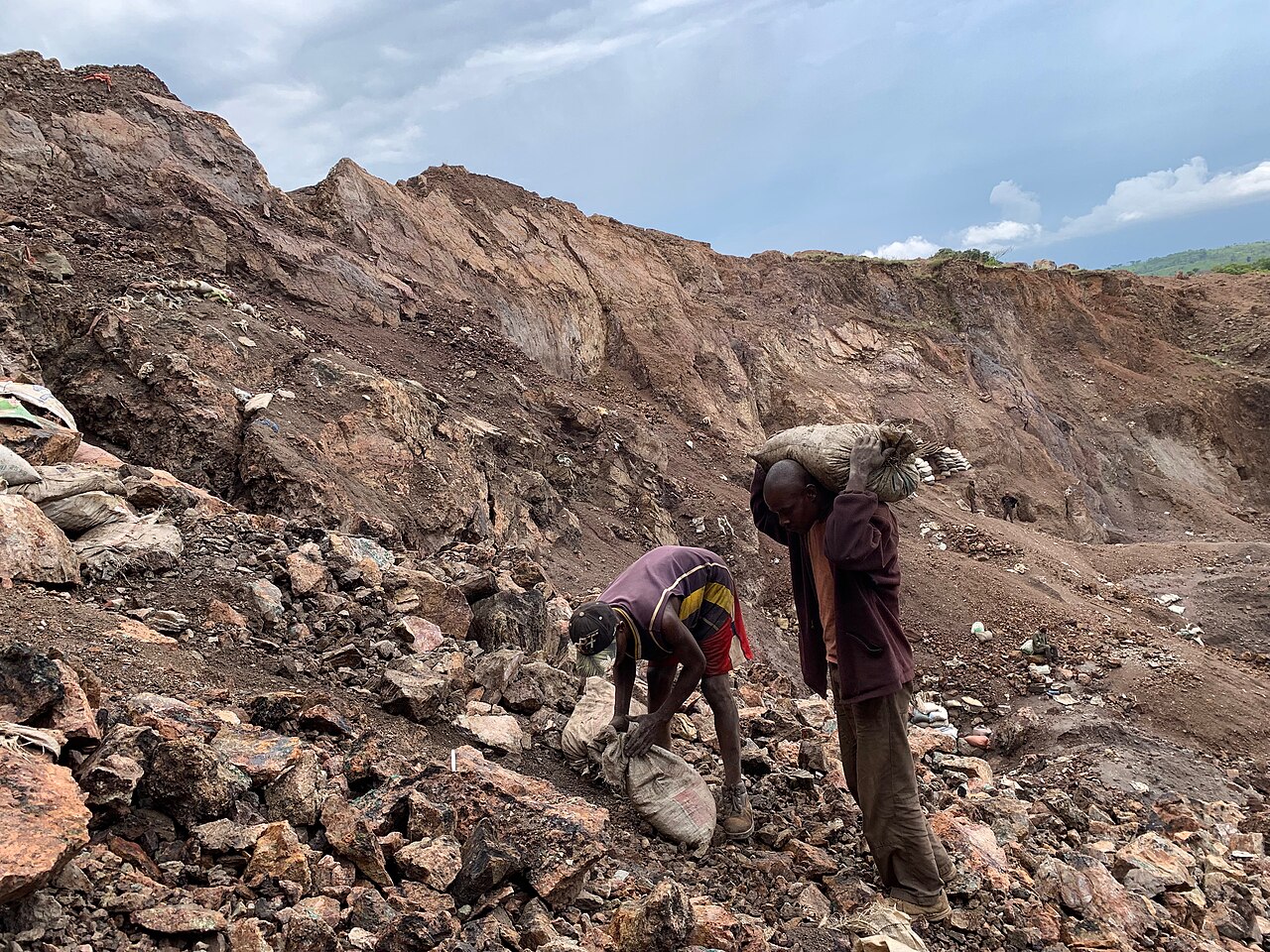 Two miners handling sacks on the rocky floor of an open artisanal cobalt mine in the Democratic Republic of the Congo, photographed in 2020.